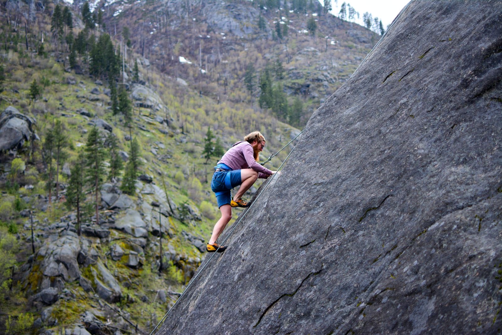 Climber on a steep granite slab in a forested mountain setting