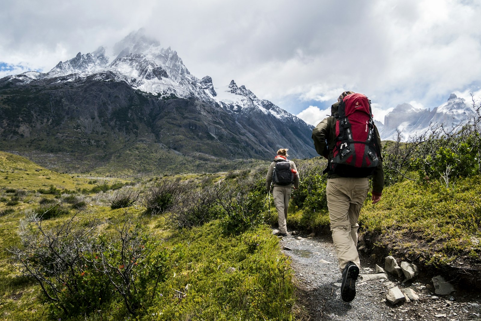 Two alpine hikers approaching a snow-capped mountain peak