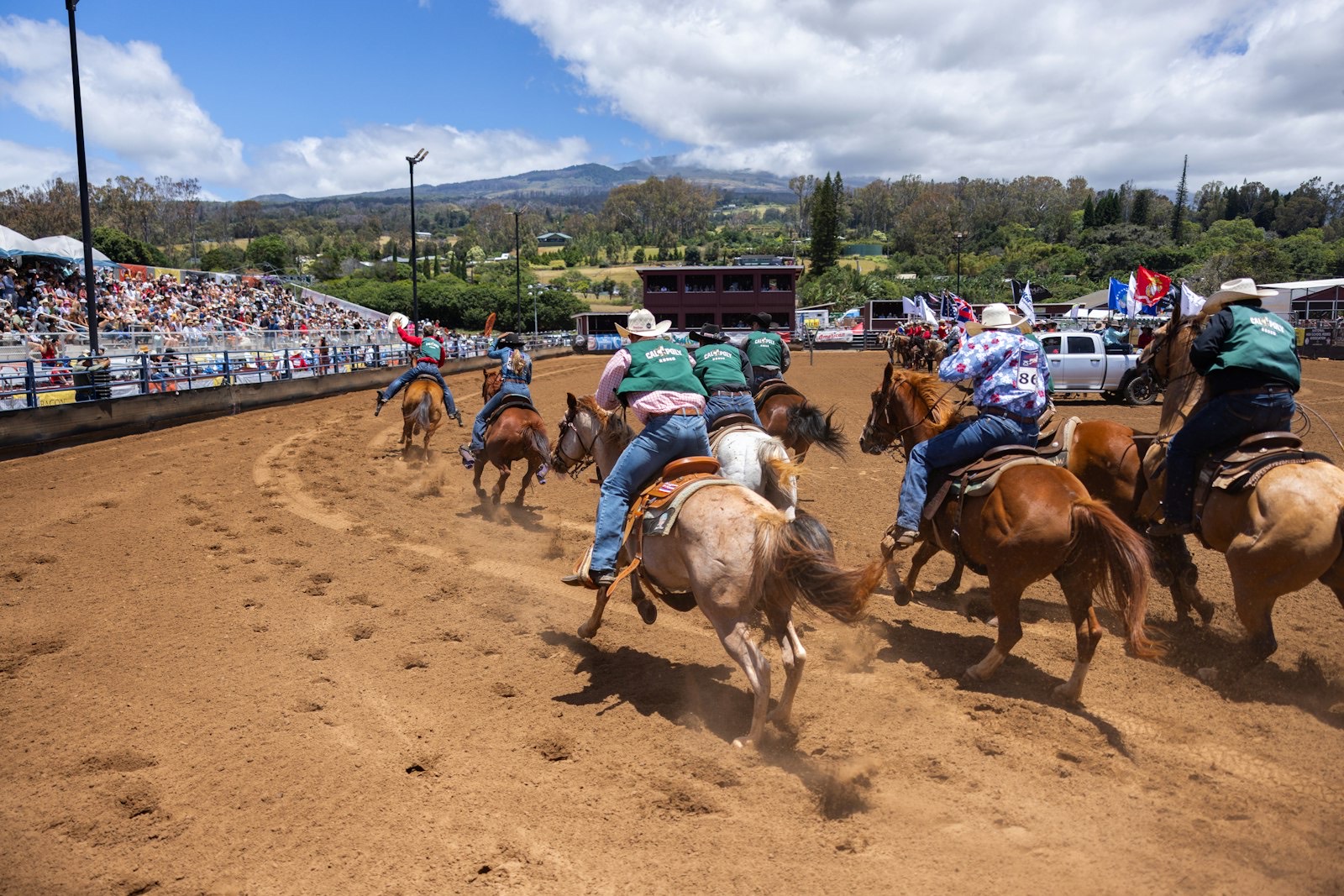 Cowboys on horseback galloping across a dirt rodeo arena
